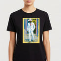 Camiseta com estampa frontal de homem de terno branco segurando bengala, chapéu elegante, ao fundo parede com graffiti e dois observadores.