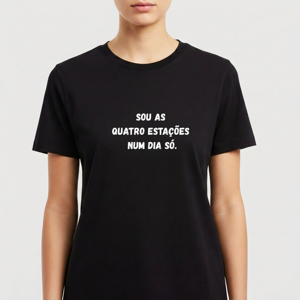 Camiseta com estampa frontal de texto em forma de frase que diz "SOU AS QUATRO ESTAÇÕES NUM DIA SÓ." em fonte de estilo marcante e legível.