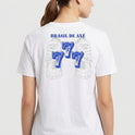 Camiseta com estampa frontal de brasão detalhado e estampa traseira de "Brasil de Axé" com números "777" estilizados sobre imagem difusa de elementos culturais.