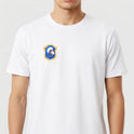 Camiseta com estampa frontal de brasão detalhado e estampa traseira de "Brasil de Axé" com números "777" estilizados sobre imagem difusa de elementos culturais.