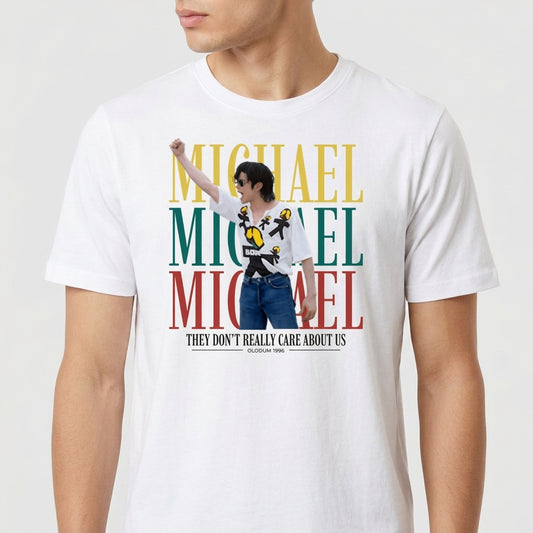 Camiseta com estampa frontal de uma pessoa de óculos em pose dinâmica, sobreposta por letras grandes "MICHAEL" em três cores e texto abaixo alusivo a uma data.
