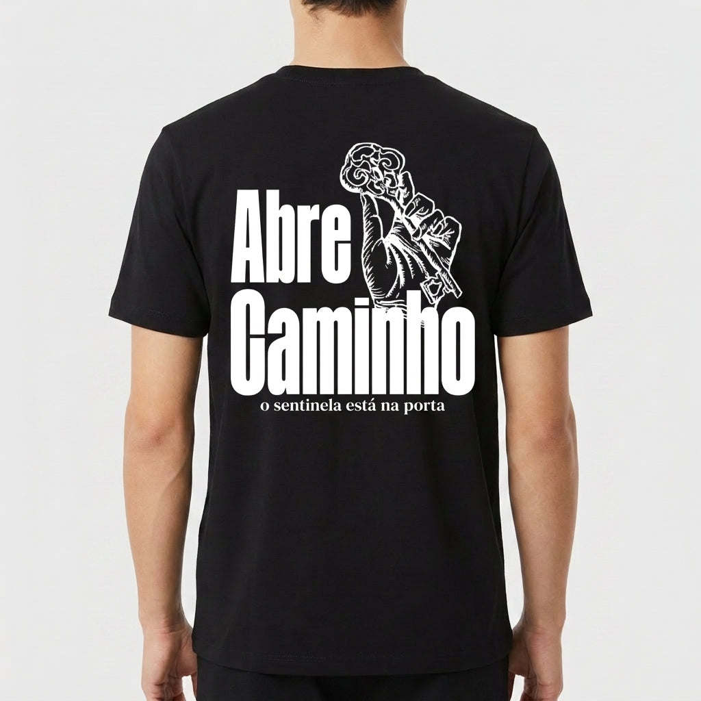 Camiseta com estampa traseira de mão segurando uma chave intricada ao lado das palavras "Abre Caminho" e uma frase menor abaixo, em estilo imponente.