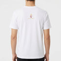 Camiseta com estampa frontal de imagem religiosa cercada por flores detalhadas e estampa traseira de logotipo estilizado com coroa e texto minimalista.